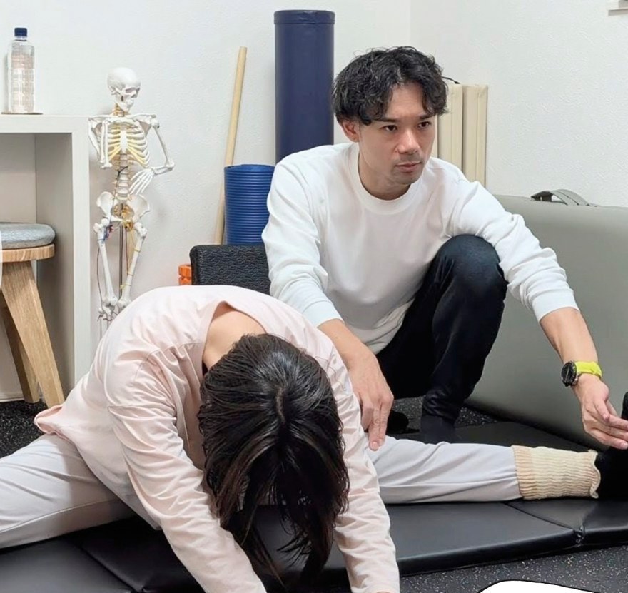 開脚前屈するお客様に、トレーナーが脚の位置を手で示している