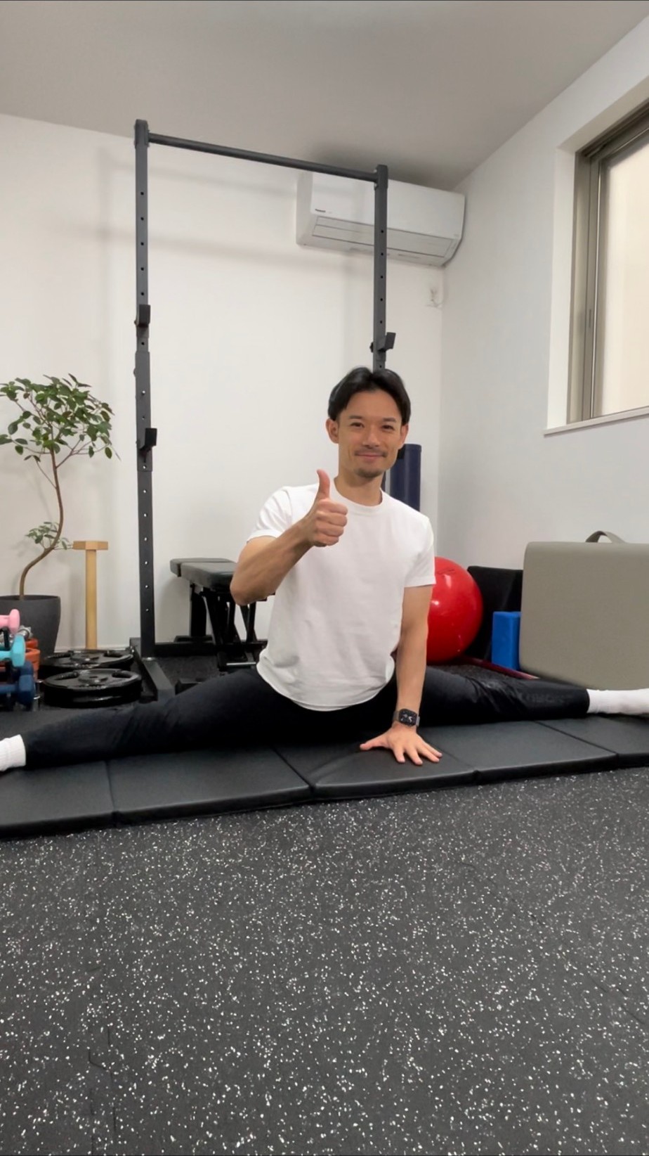 開脚しながら親指を立てて笑うトレーナー